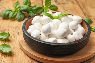 Photo of Mozzarella cheese balls and basil on wooden table, closeup