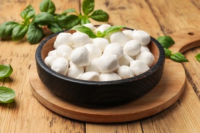 Photo of Mozzarella cheese balls and basil on wooden table, closeup