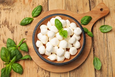 Photo of Mozzarella cheese balls and basil on wooden table, flat lay