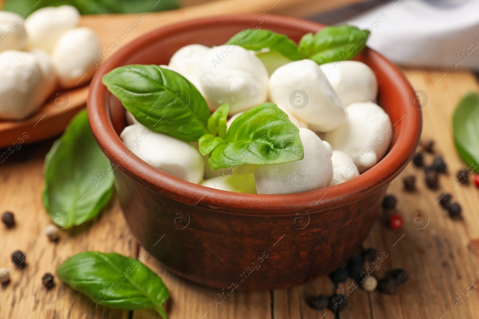 Mozzarella cheese balls with basil and peppercorns on wooden table, closeup Photo of Mozzarella cheese balls with basil and peppercorns on wooden table, closeup