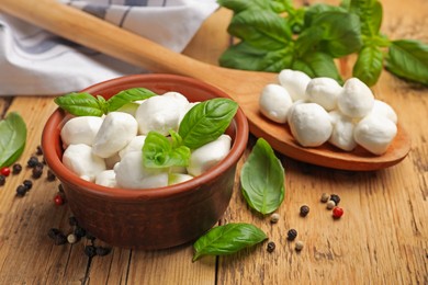 Photo of Mozzarella cheese balls with basil and peppercorns on wooden table, closeup