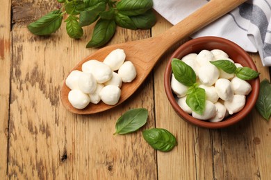 Photo of Mozzarella cheese balls and basil on wooden table, flat lay