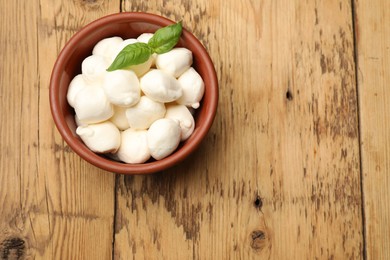 Photo of Mozzarella cheese balls and basil on wooden table, top view. Space for text