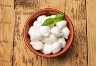 Photo of Mozzarella cheese balls and basil on wooden table, top view