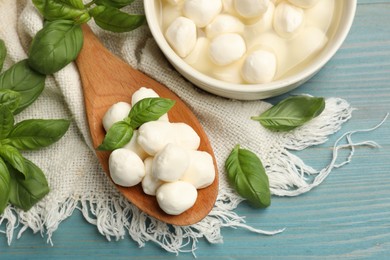 Photo of Mozzarella cheese balls and basil on blue wooden table, flat lay