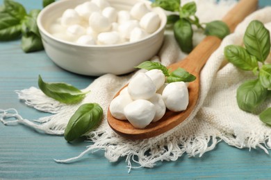 Photo of Mozzarella cheese balls and basil on blue wooden table, closeup