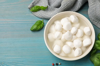 Photo of Mozzarella cheese balls with basil and peppercorns on blue wooden table, flat lay. Space for text