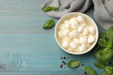 Photo of Mozzarella cheese balls with basil and peppercorns on blue wooden table, flat lay. Space for text