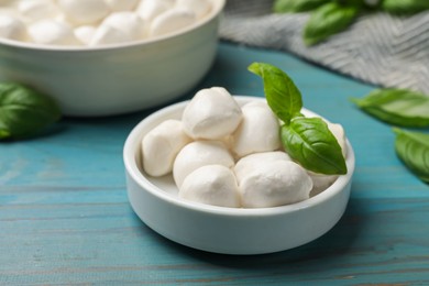 Photo of Mozzarella cheese balls and basil on blue wooden table, closeup