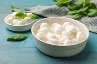 Photo of Mozzarella cheese balls and basil on blue wooden table, closeup