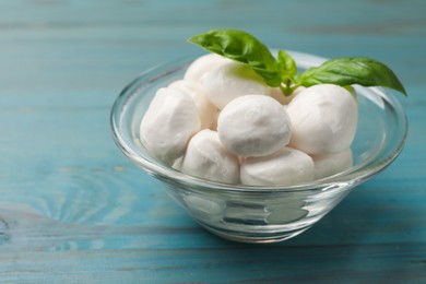 Photo of Mozzarella cheese balls and basil on blue wooden table, closeup