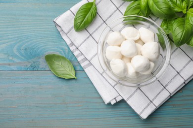 Photo of Mozzarella cheese balls and basil on blue wooden table, flat lay