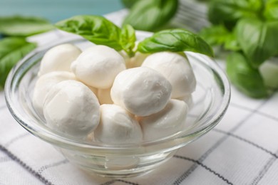 Photo of Mozzarella cheese balls and basil on blue table, closeup