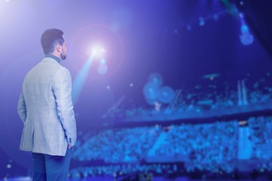 Image of Man performing on stage of concert hall crowded with people
