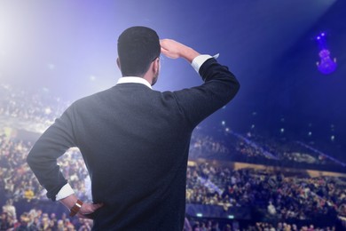 Image of Man performing on stage of concert hall crowded with people