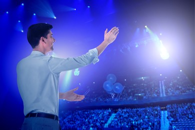 Image of Man performing on stage of concert hall crowded with people