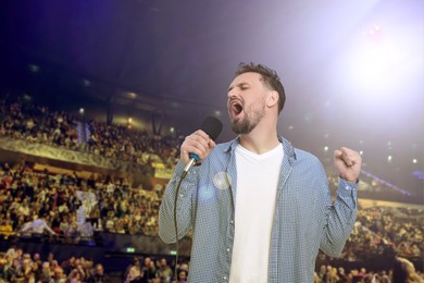 Image of Man singing on stage of concert hall crowded with people