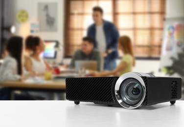 Image of Modern video projector on white table and people working in conference room, selective focus