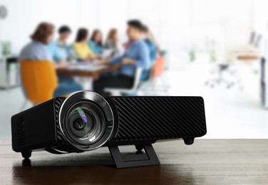 Image of Modern video projector on wooden table and people working in conference room, selective focus