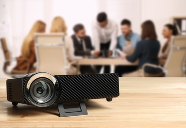Image of Modern video projector on wooden table and people working in conference room, selective focus
