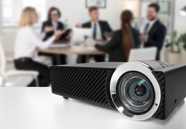 Image of Modern video projector on white table and people working in conference room, selective focus