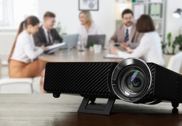 Image of Modern video projector on wooden table and people working in conference room, selective focus