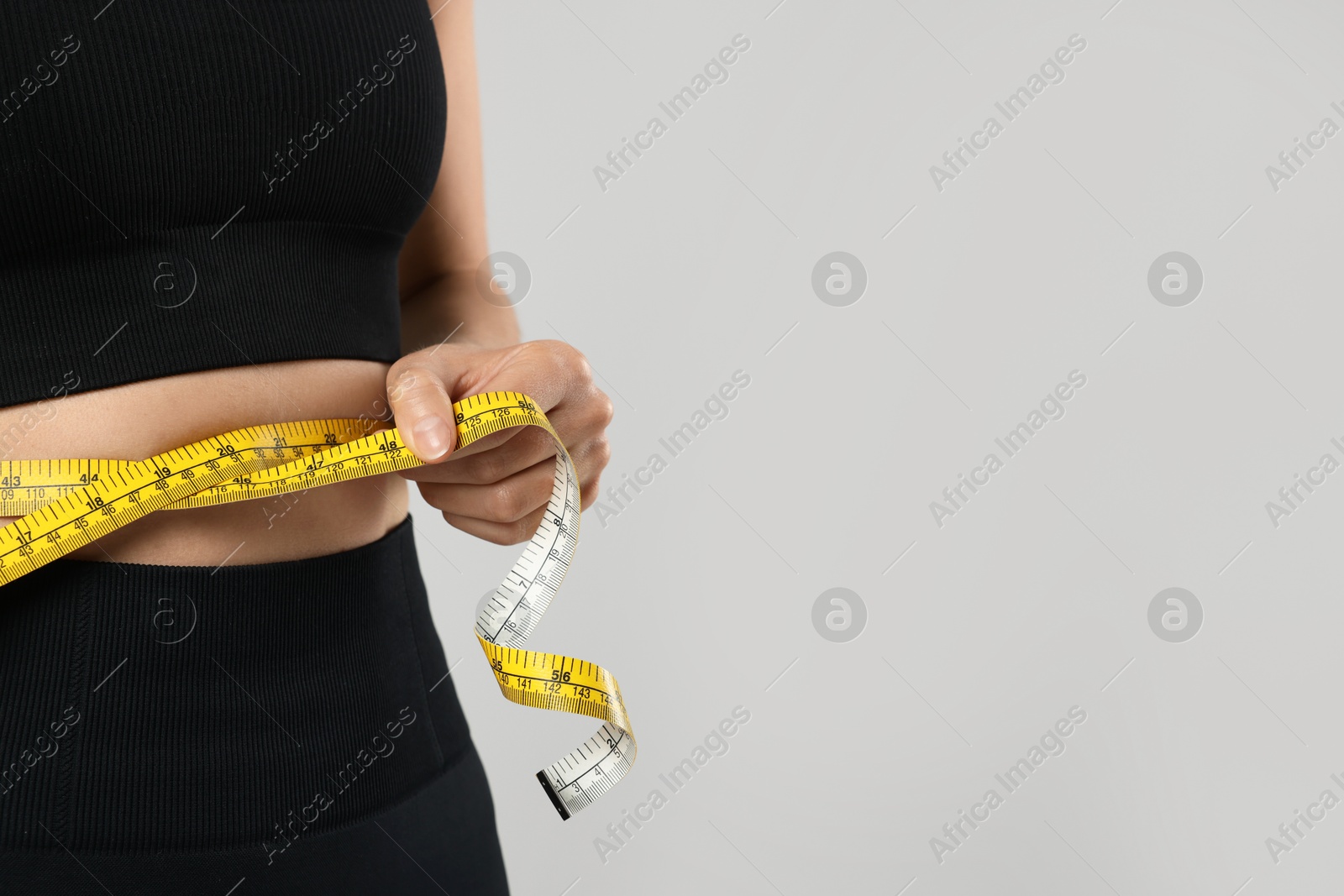 Woman measuring her belly with tape on gray background, closeup. Space for text Photo of Woman measuring her belly with tape on gray background, closeup. Space for text