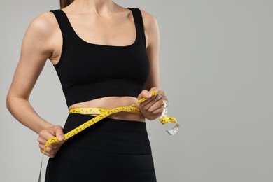 Photo of Woman measuring her belly with tape on gray background, closeup. Space for text