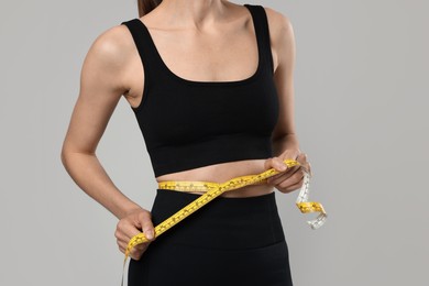 Photo of Woman measuring her belly with tape on gray background, closeup