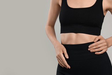 Photo of Beautiful woman with flat belly on gray background, closeup. Space for text
