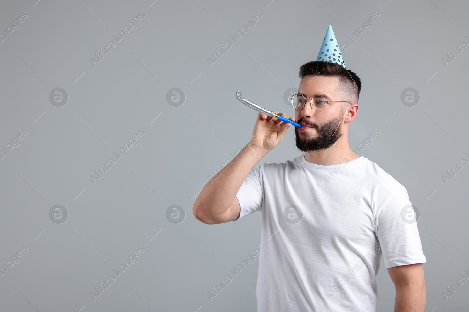 Happy Birthday. Handsome man with party hat and blower on grey background, space for text Photo of Happy Birthday. Handsome man with party hat and blower on grey background, space for text