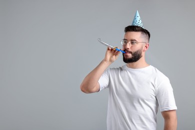 Photo of Happy Birthday. Handsome man with party hat and blower on grey background, space for text