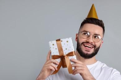Photo of Happy Birthday. Handsome man with party hat and gift box on grey background, space for text