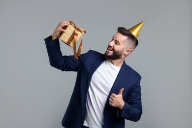 Photo of Happy Birthday. Handsome man with party hat and gift box showing thumbs up on grey background