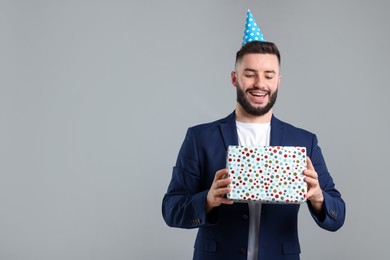 Photo of Happy Birthday. Handsome man with party hat and gift box on grey background, space for text