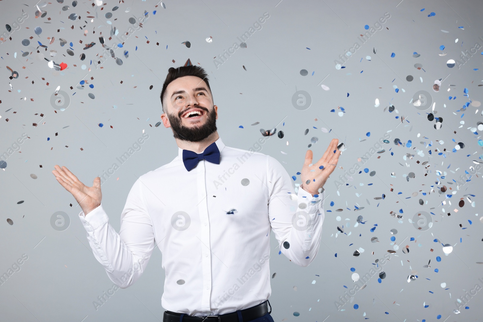 Happy Birthday. Handsome man with party hat under confetti shower on grey background, space for text Photo of Happy Birthday. Handsome man with party hat under confetti shower on grey background, space for text