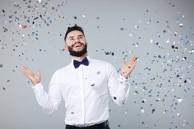 Photo of Happy Birthday. Handsome man with party hat under confetti shower on grey background, space for text