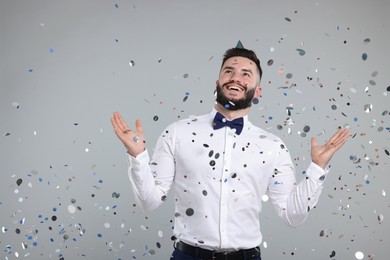 Photo of Happy Birthday. Handsome man with party hat under confetti shower on grey background, space for text