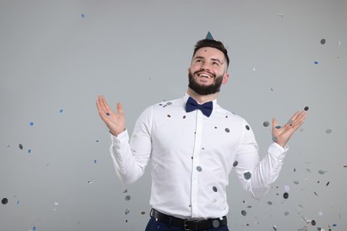 Photo of Happy Birthday. Handsome man with party hat under confetti shower on grey background, space for text