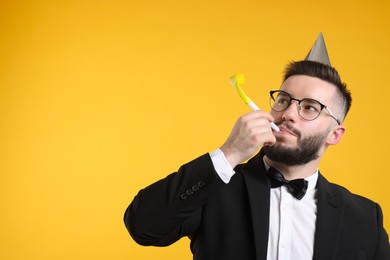 Photo of Happy Birthday. Handsome man with party hat and blower on orange background, space for text