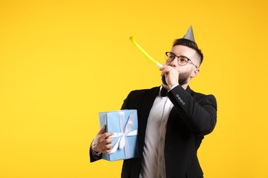 Photo of Happy Birthday. Handsome man with party hat, blower and gift box on orange background, space for text