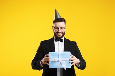 Photo of Happy Birthday. Handsome man with party hat and gift box on orange background