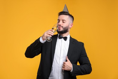 Photo of Happy Birthday. Handsome man with party hat and champagne showing thumbs up on orange background
