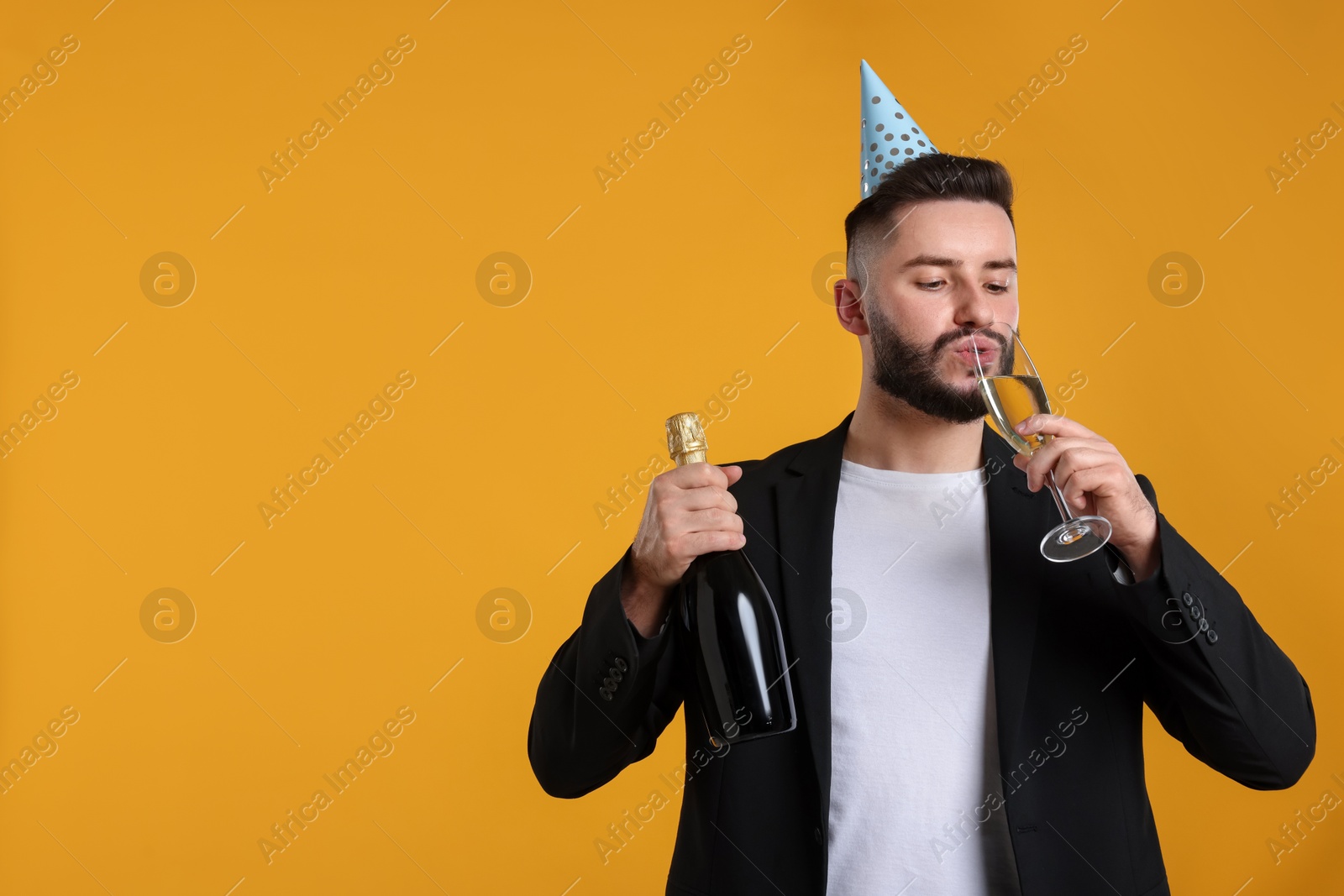 Happy Birthday. Handsome man with party hat and champagne on orange background, space for text Photo of Happy Birthday. Handsome man with party hat and champagne on orange background, space for text