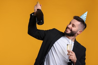 Photo of Happy Birthday. Handsome man with party hat and champagne on orange background, space for text