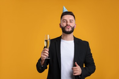 Photo of Happy Birthday. Handsome man with party hat and champagne showing thumbs up on orange background