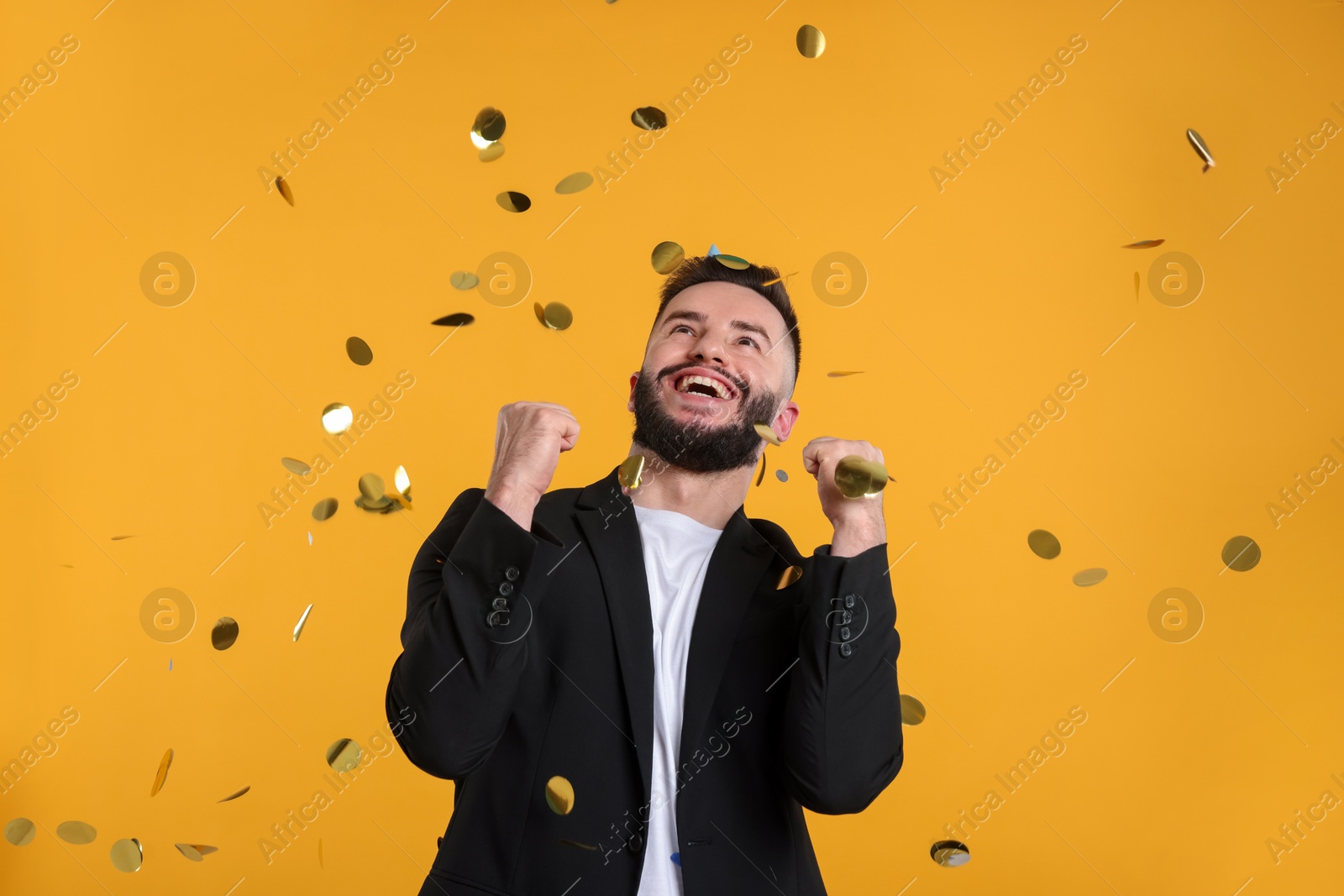 Happy Birthday. Handsome man under confetti shower on orange background Photo of Happy Birthday. Handsome man under confetti shower on orange background