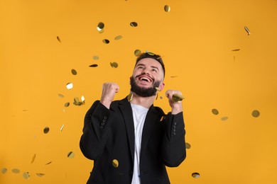 Photo of Happy Birthday. Handsome man under confetti shower on orange background