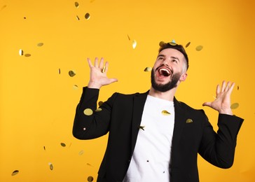 Photo of Happy Birthday. Handsome man under confetti shower on orange background, space for text