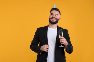 Photo of Happy Birthday. Handsome man with party hat and glass of champagne on orange background, space for text